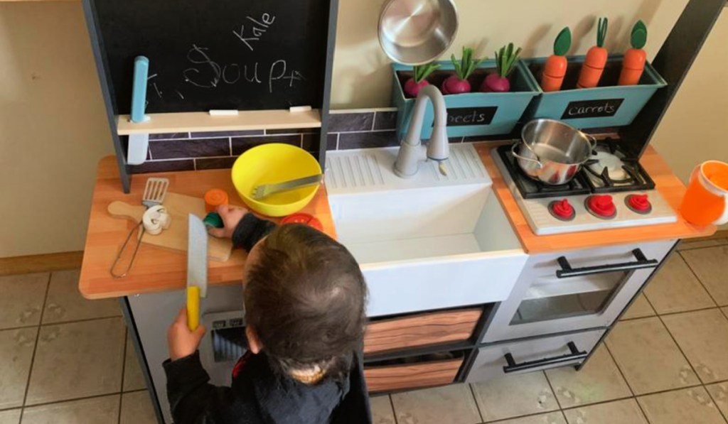 Little boy playing with kid craft wooden kitchen
