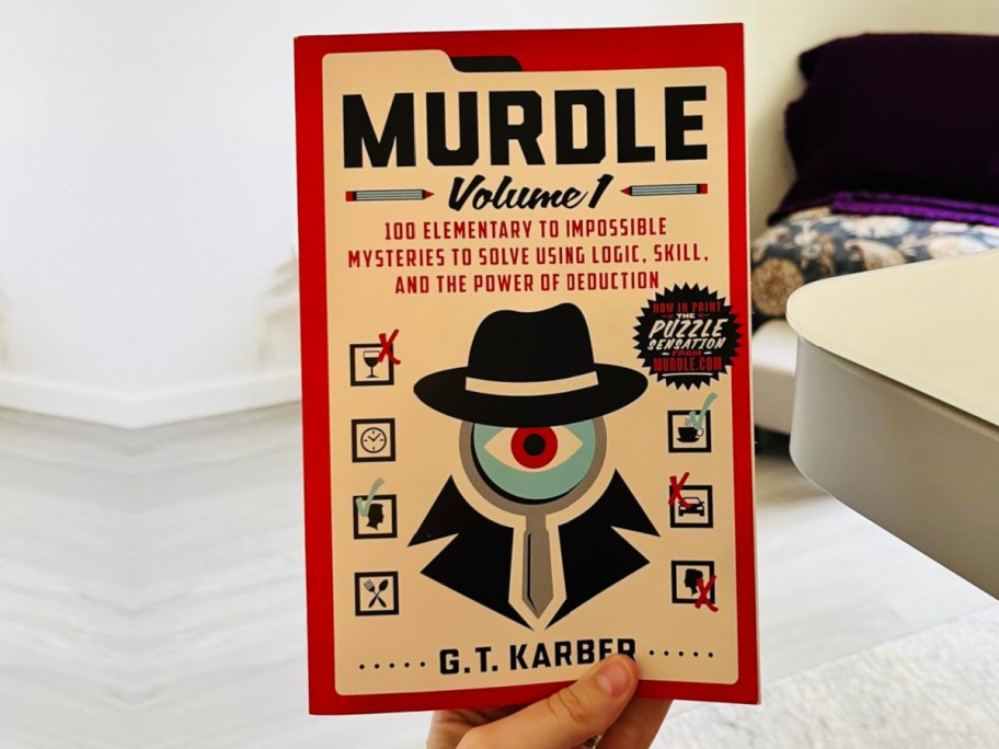 Woman holding up Murdle paperback book