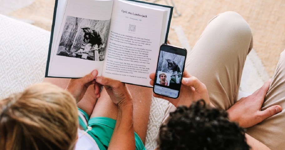Two people sitting on couch with open hardcover book and phone in hand