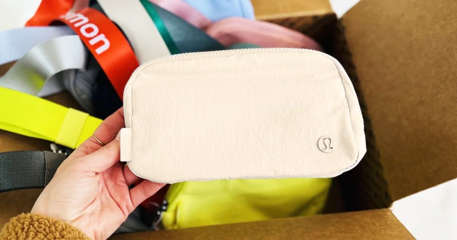 woman holding up a cream colored lululemon belt bag