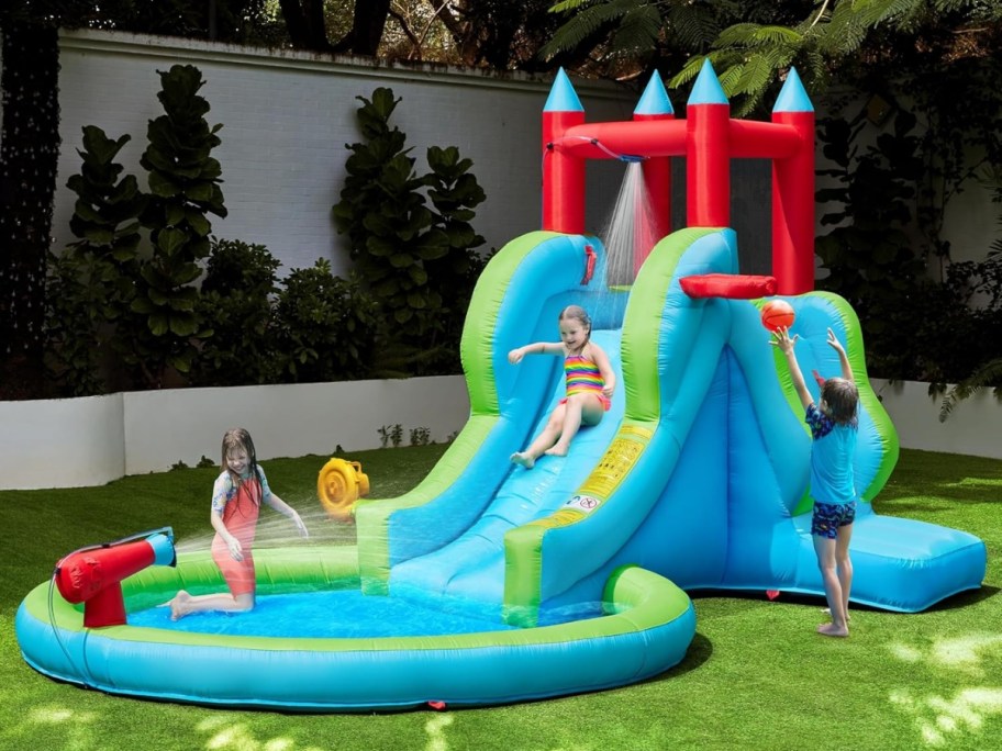 kids playing on a huge inflatable water slide in a backyard