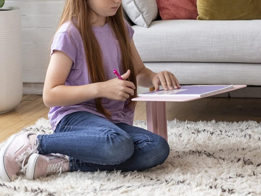 girl using a pink lap desk while sitting on the floor
