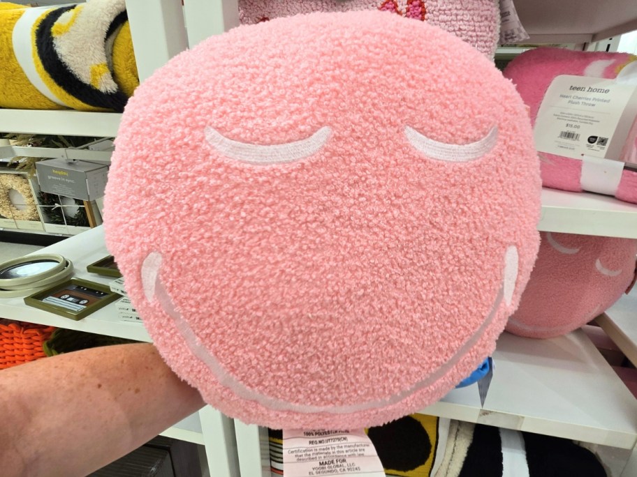 hand holding a pink round throw pillow with a smiley face on it