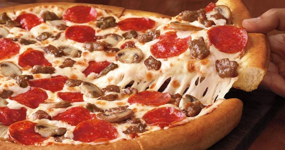hand taking a slice from a Pizza Hut Pizza with pepperoni, mushrooms, and sausage on it
