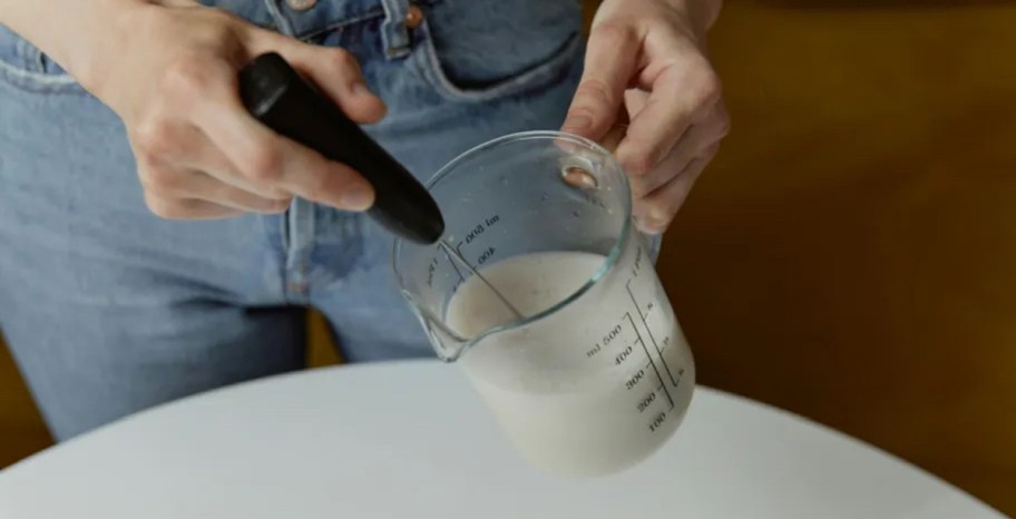 hand holding milk frother in measuring cup with milk