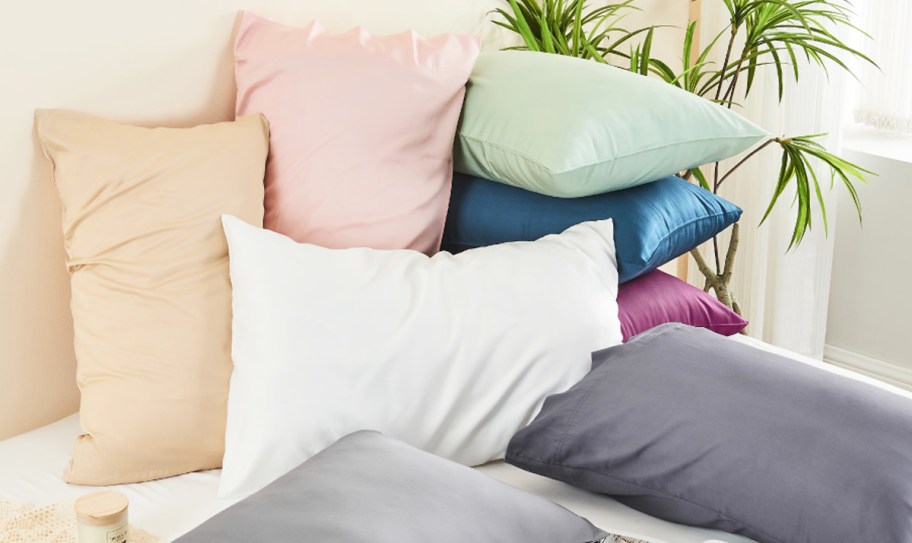 multiple pillows in different colored pillow cases on a bed