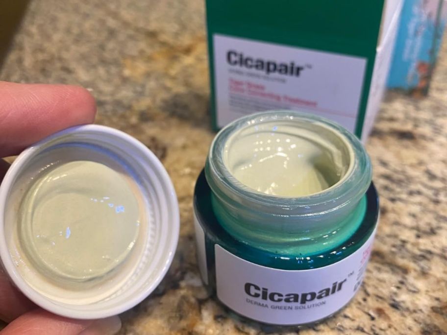A person opening a jar of Dr. Jart+ Cicapair Soothing Color Correcting Treatment