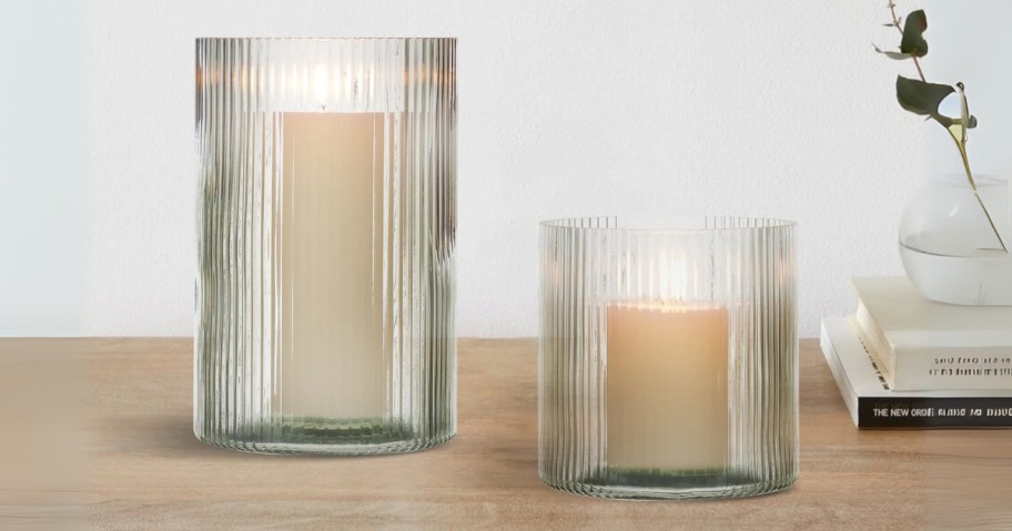 2 clear glass ribbed candle holders in different sizes on a mantle