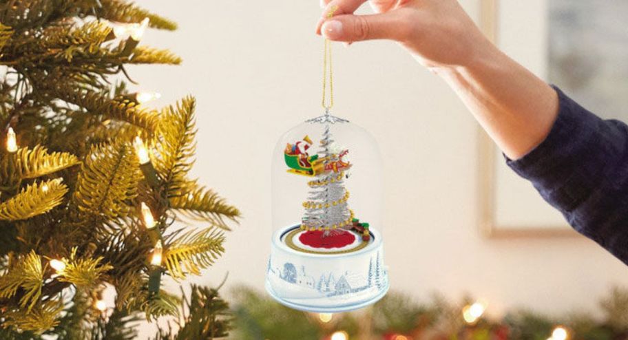 hand holding new hallmark ornament up to christmas tree