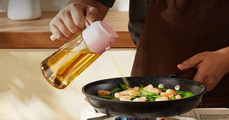 person using olive oil dispenser with pink top to spray skillet full of food