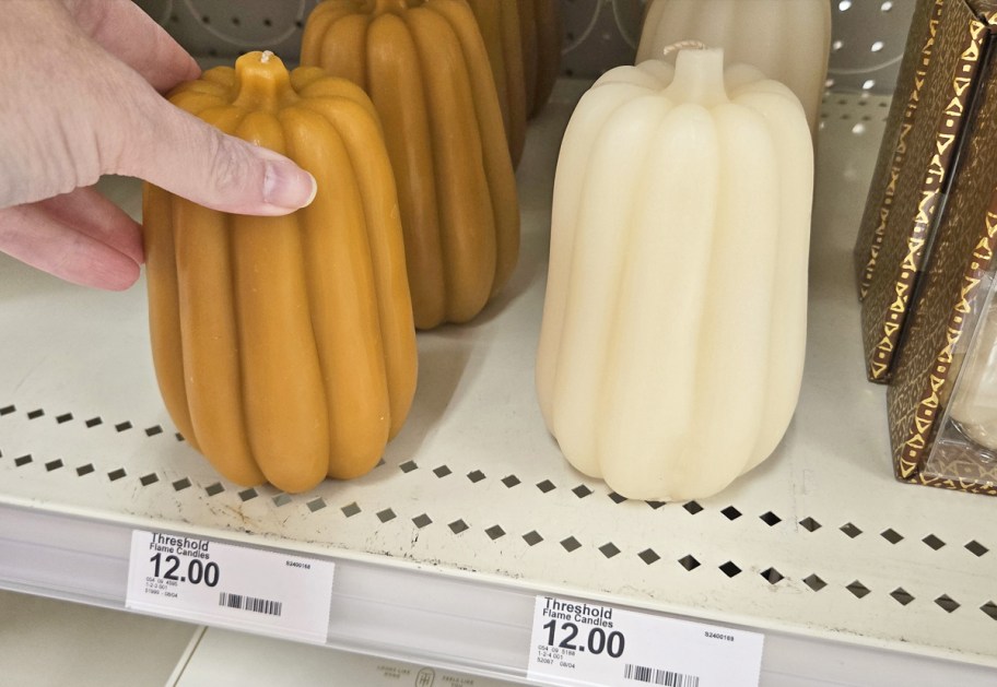 hand touching pumpkin shaped candles on store shelf
