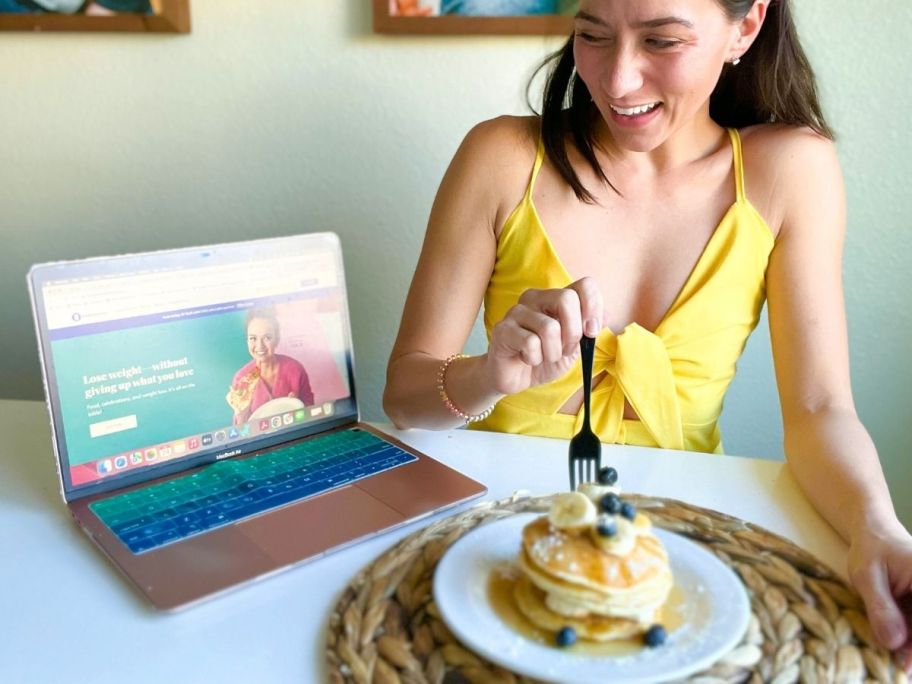 Woman with a plate of pancakes with computer on Weight Watchers website