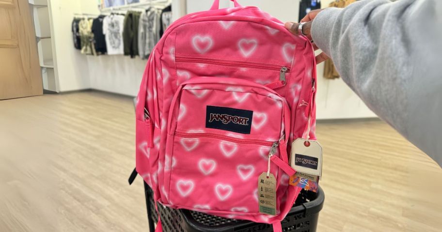 pink jansport backpack with hearts on it in hand in store