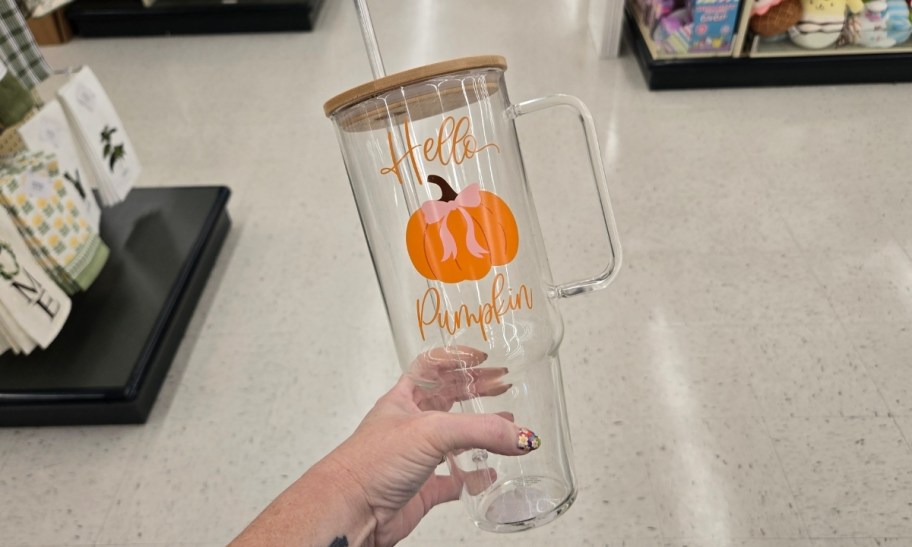a womans hand holding a glass tumbler with lid and straw