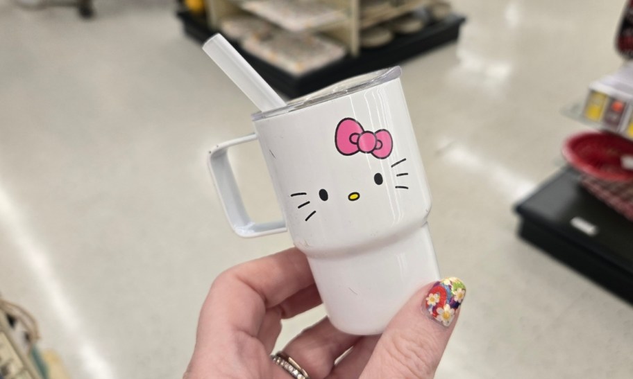 a womans hand holding a white hello kitty mini tumbler