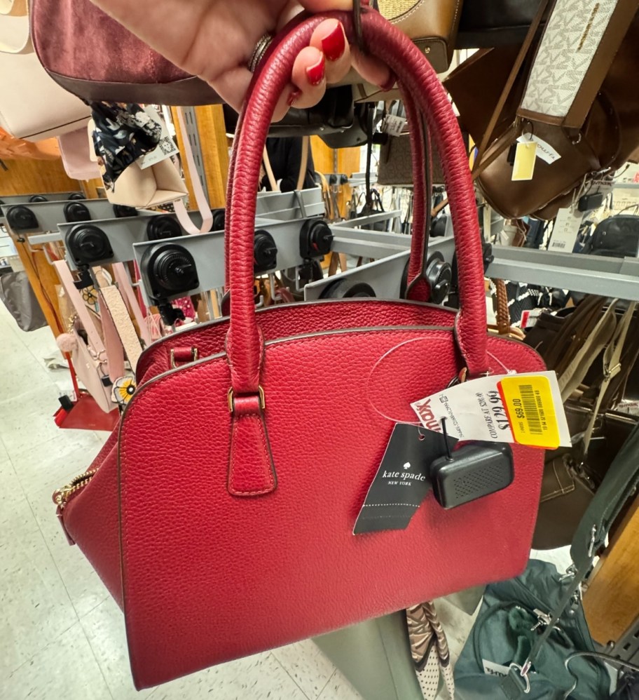 womans hand holding the top handles of a red handbag