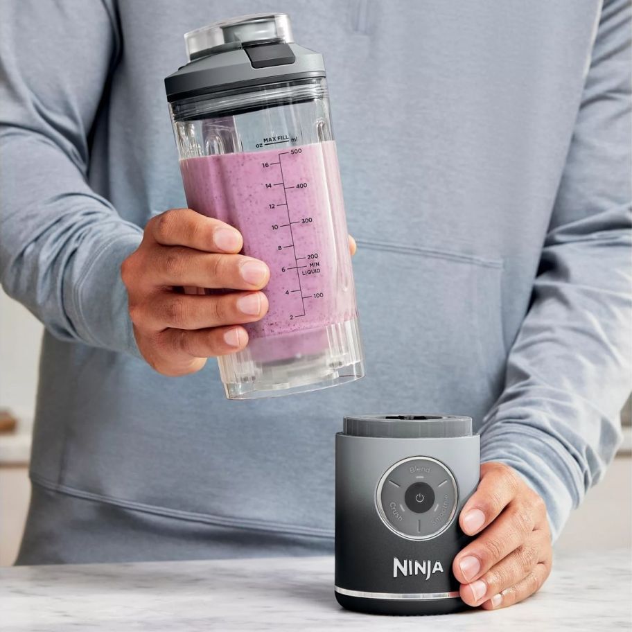 a man holding the ninja blast max blender base in one hand and the blend cup in the other