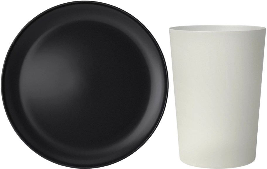 A black round plate and a beige cylindrical cup are placed side by side against a plain background.