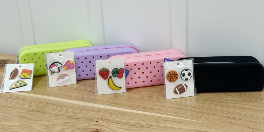 green, purple, pink, and black pencil cases with charms on table