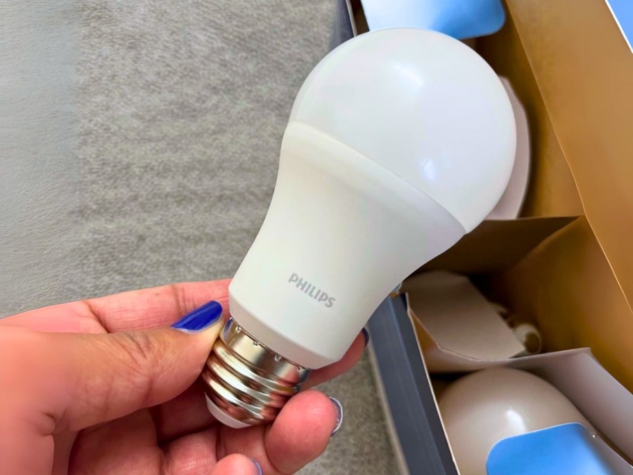 hand holding a Philips light bulb, boxes of more bulbs behind it