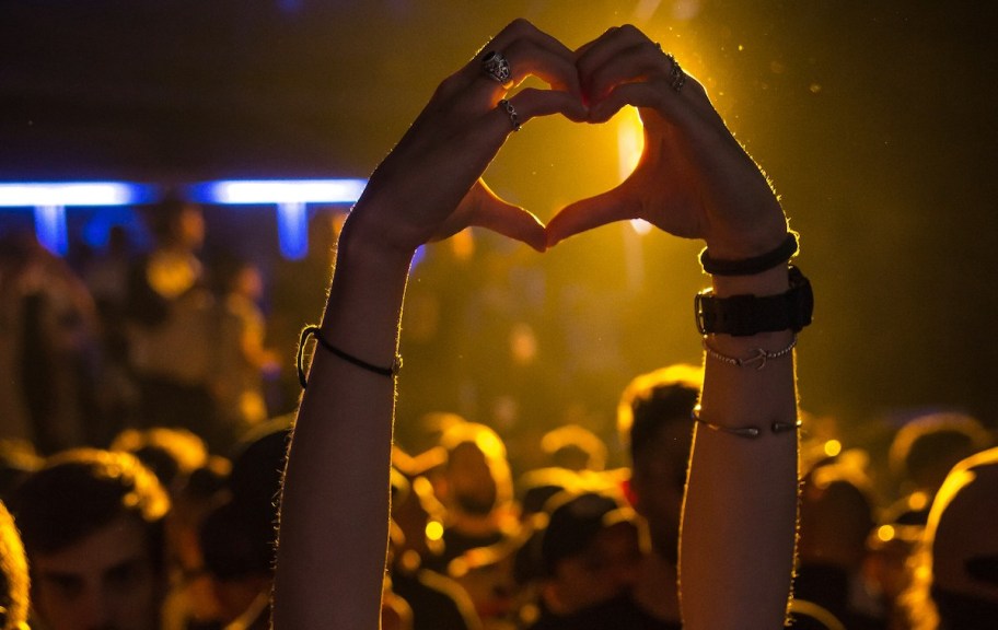 Person holding up hands in shape of a heart at concert 