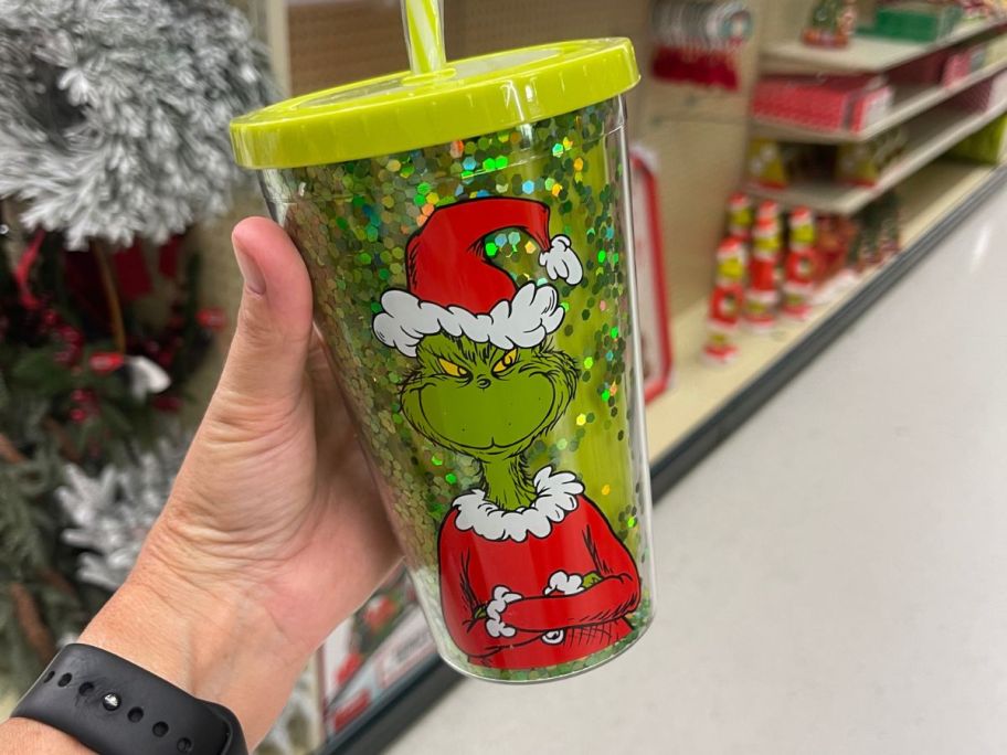 A person holding a green drink tumbler with the Grinch's face on it 