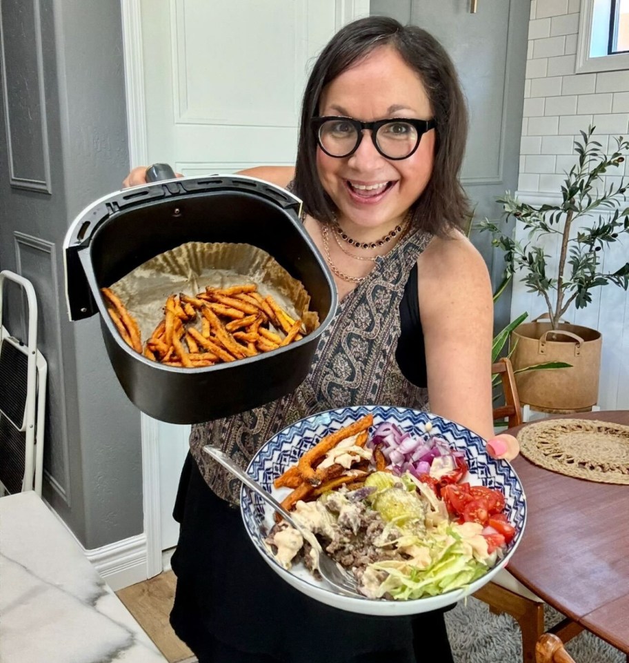 woman holding sweet potato fries in the air fryer and a burger bowl 