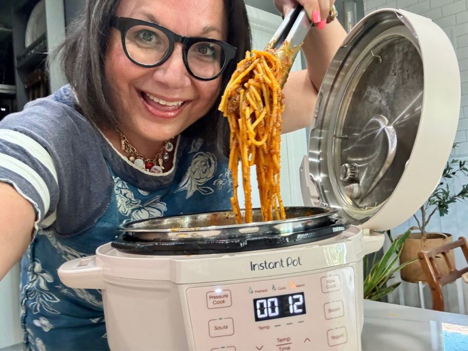 Woman holding tongs full of spaghetti over an Instant Pot Mini