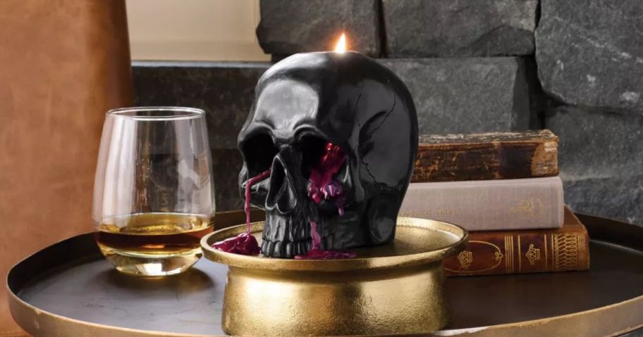 A black skull candle "bleeding" while melting on a table with a drink