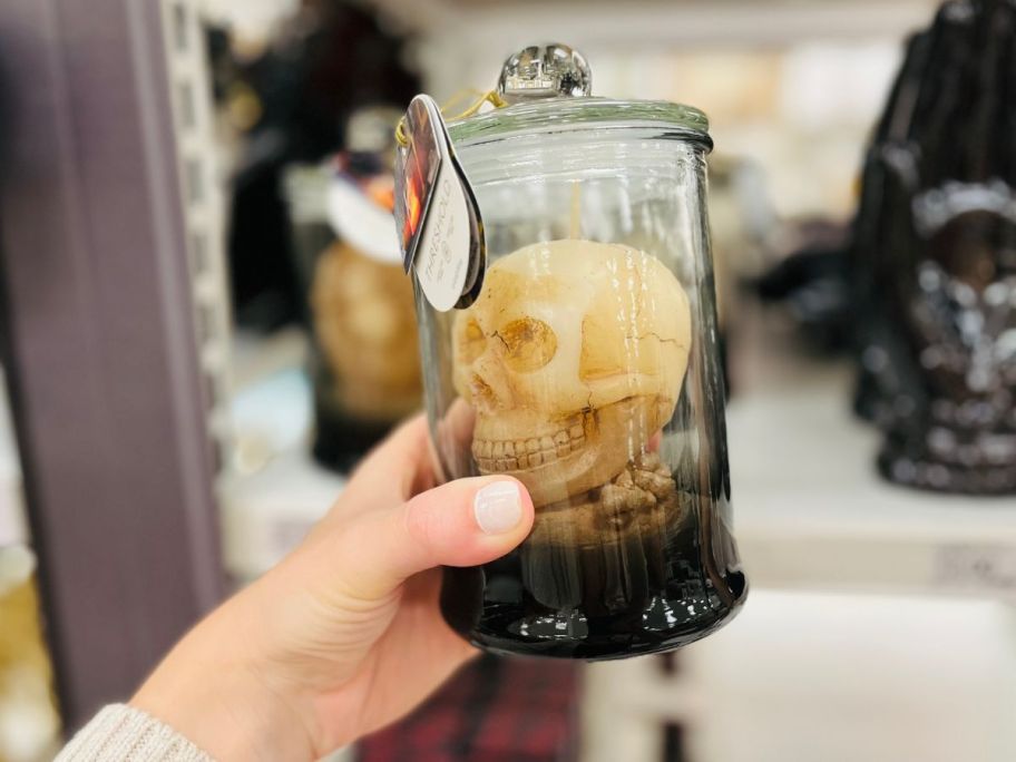 a hand holding a skull figural candle under a cloche 