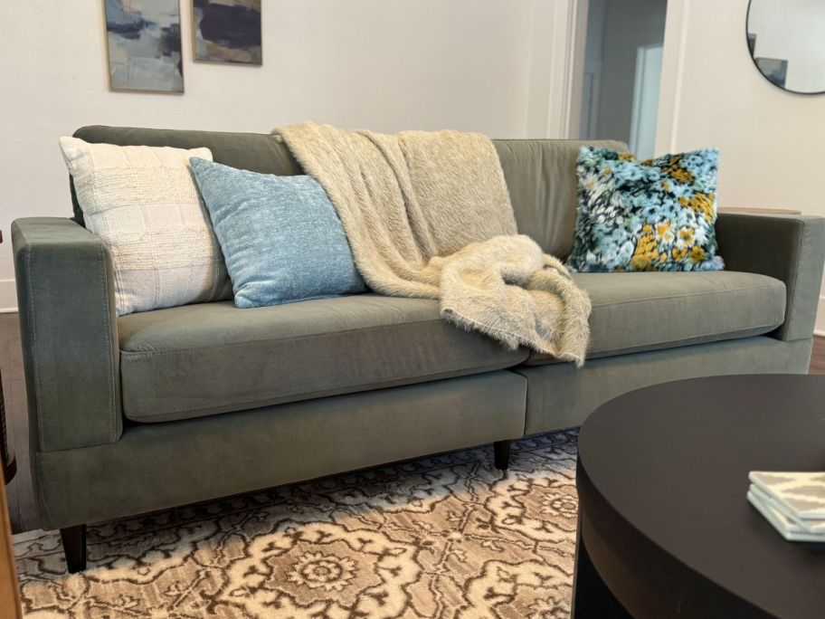 A gray Better Homes & Gardens Springwood Wood Frame Couch with throw pillows and a blanket on it