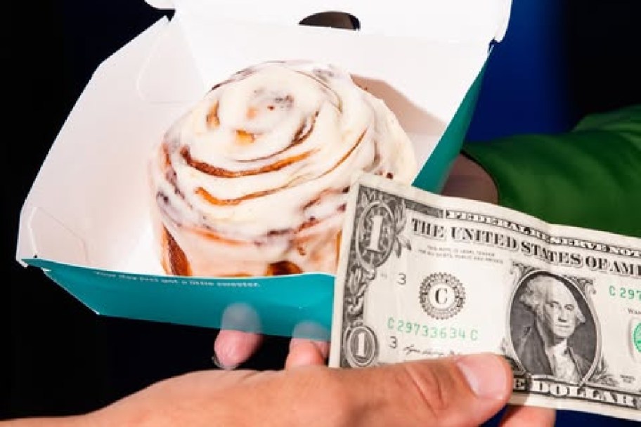cinnabon cinnamon roll and a dollar in hand