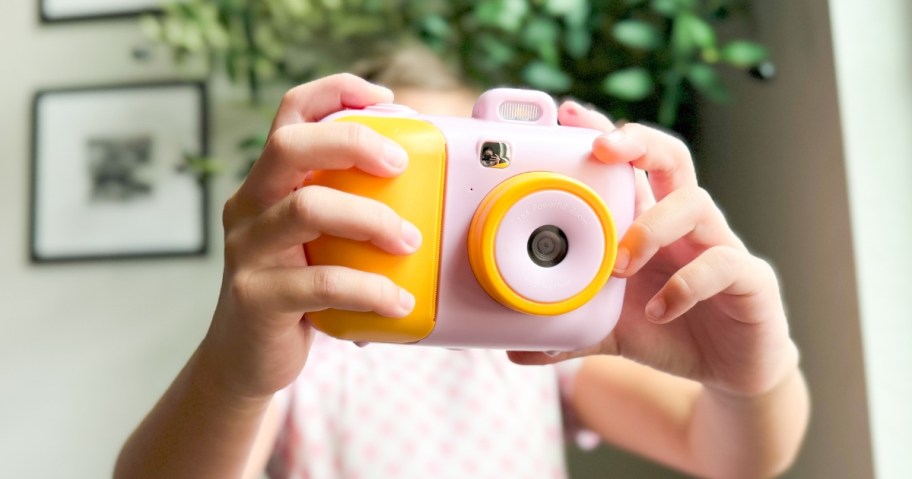 a girl holding up a pink and orange kids digital camera