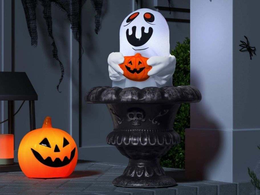 Rising Porch Pot Ghost Halloween Decorative Prop displayed next to a pumpkin on the porch