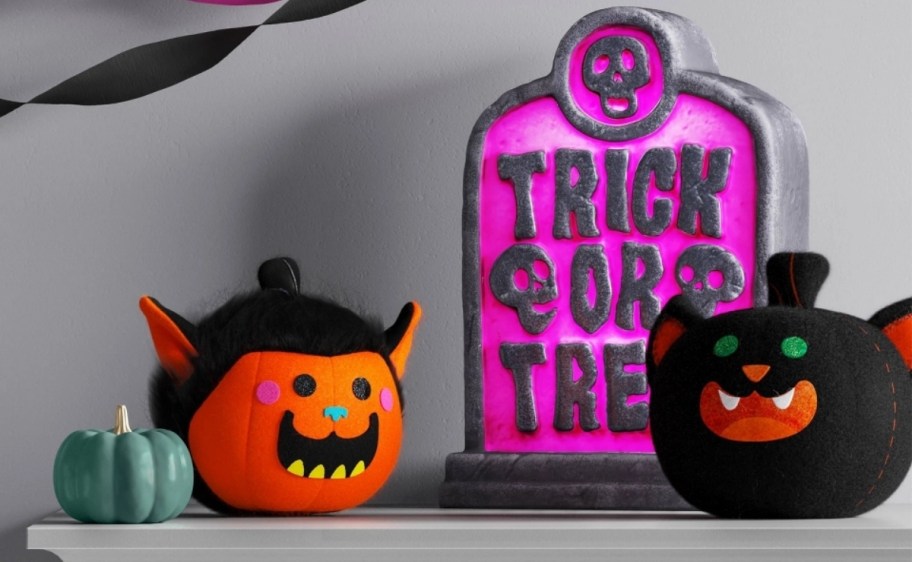 two felt pumpkin figures and a purple trick or treat blow mold on a fireplace mantle