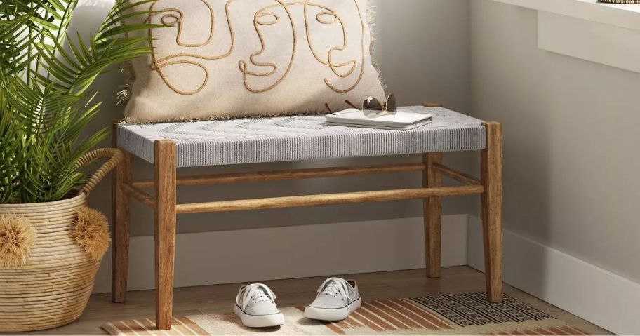 An entryway bench with a pillow on top of it and a pair of shoes beneath it 