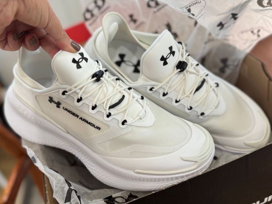 Hand touching a pair of Under Armour shoes in a shoebox