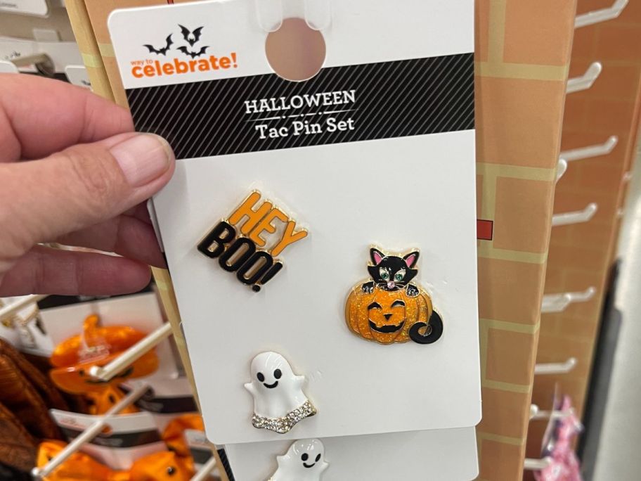A person holding a trio of Halloween pins at Walmart: Hey Boo, Cat & Pumpkin, & Ghost