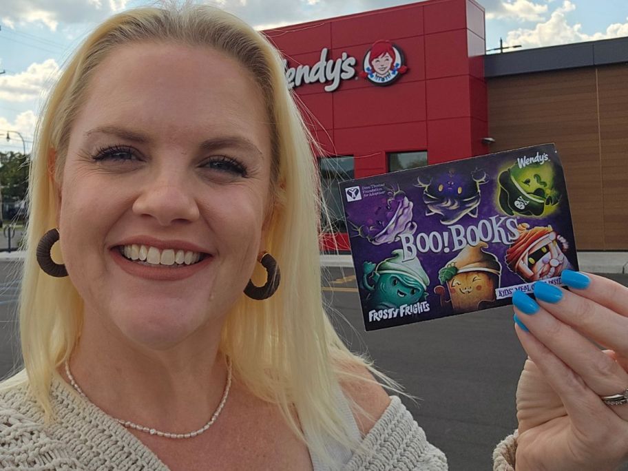 A woman holding a Wendy's coupon book in front of a Wendy's