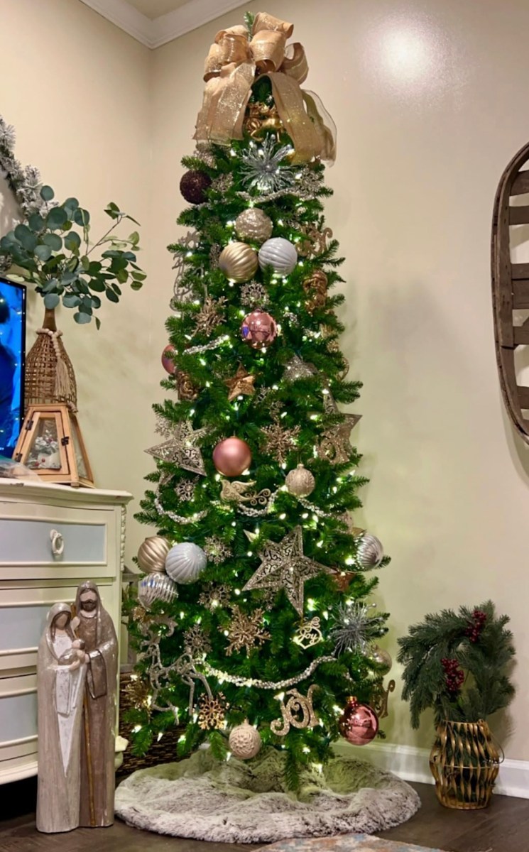 slim christmas tree decked out with pink and silver ornaments in corner of room