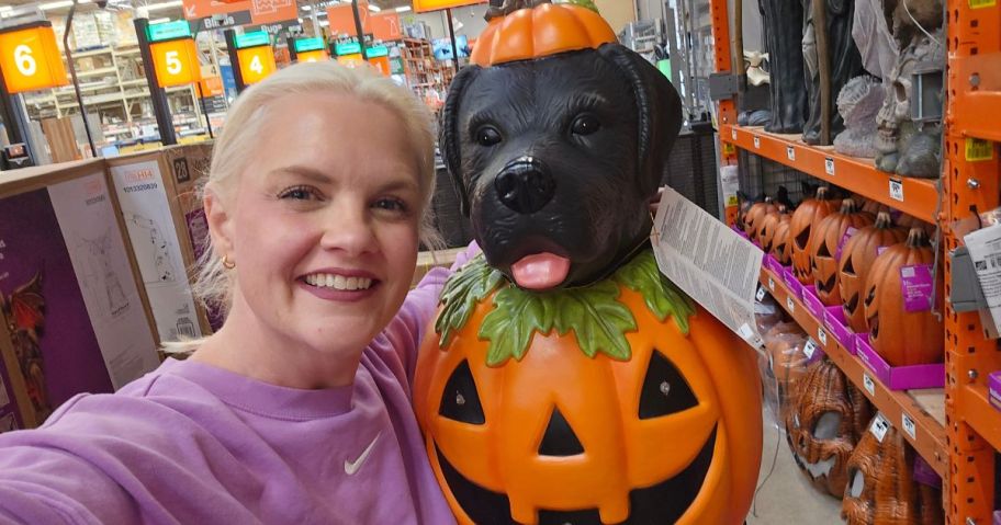 woman holding labrador blow mold wearing a pumpkin costume in store