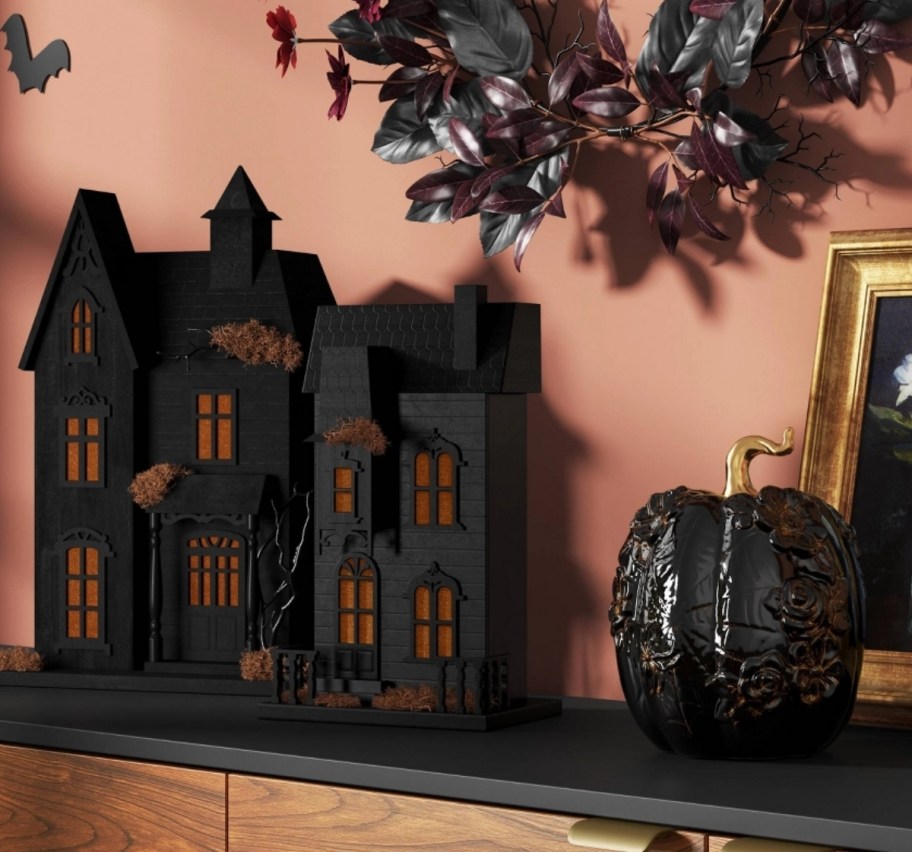 two lit haunted houses shown with a large ceramic pumpkin