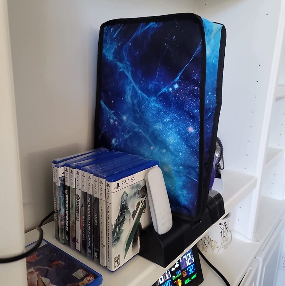 Galaxy printed PlayStation dust cover on gaming console sitting on shelf with PS5 games 