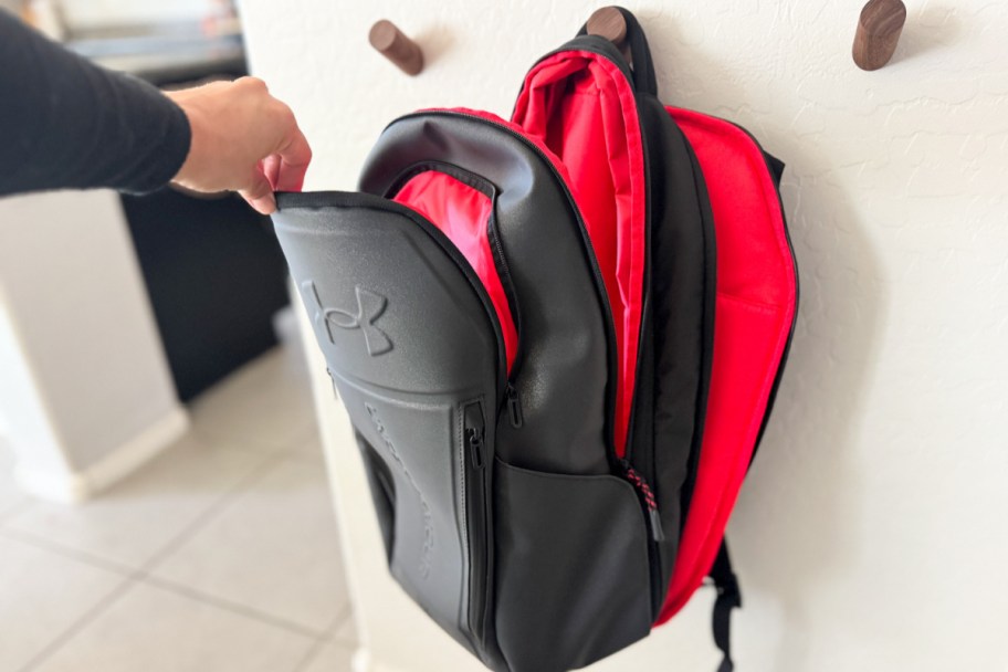 hand grabbing black backpack unzipped on wood hanger