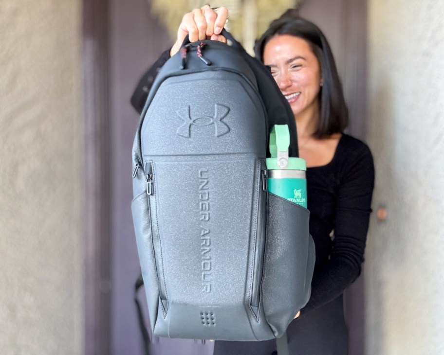 woman holding black backpack in front of door