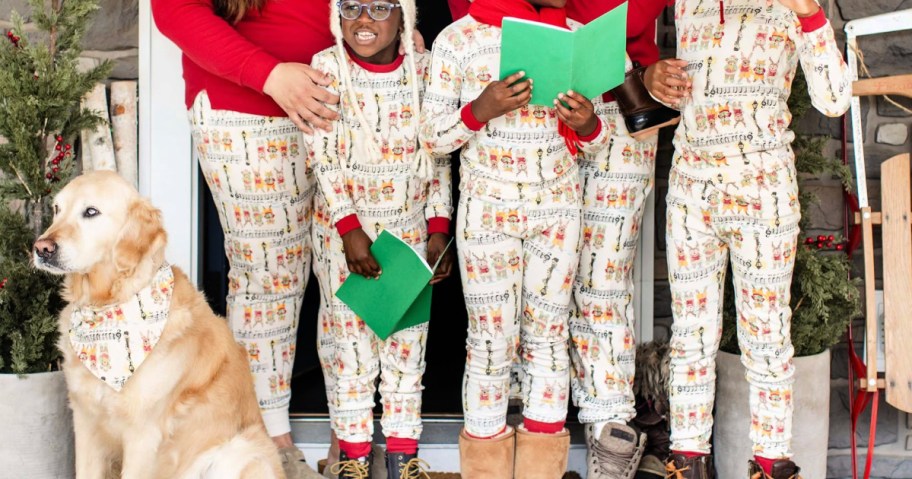 Family wearing matching holiday pajamas, while standing outside and caroling