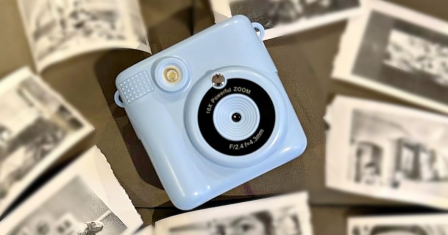 A pastel blue vintage-style camera lies on a surface surrounded by scattered black-and-white photos.