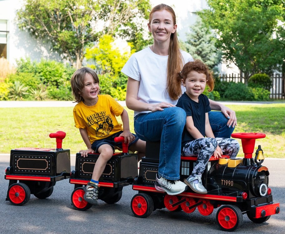 mom and two kids sitting on a black and red train ride-on toy