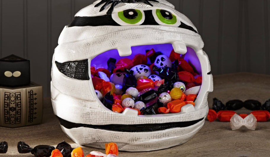 Mummy candy bowl filled with Halloween candy on wooden countertop