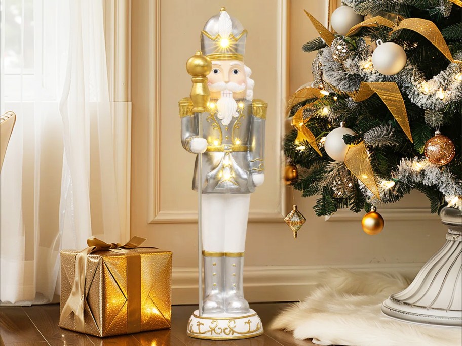 silver and gold nutcracker near a christmas tree